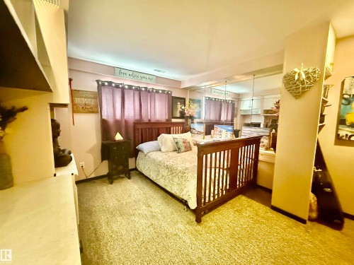 Carpeted room featuring a wooden bed frame, mirrored wall paneling, and a window with drapes - 3520 17B Avenue, Edmonton, AB - Indoor Photo Showing Bedroom
