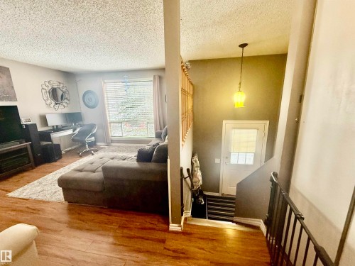 Living area with wood-finish flooring, a large window, and a textured ceiling - 3520 17B Avenue, Edmonton, AB - Indoor Photo Showing Living Room