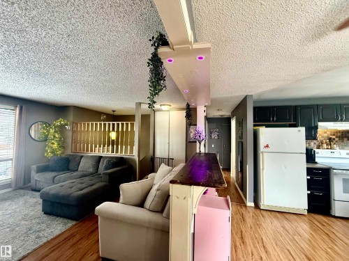 Open-concept living space featuring wood-finish flooring, a kitchen with dark cabinetry, and a partial wall with wooden slat detailing - 3520 17B Avenue, Edmonton, AB - Indoor