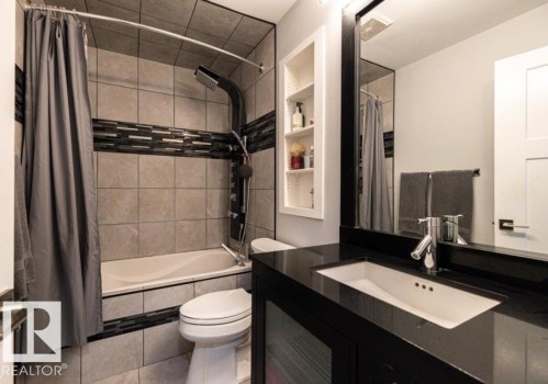This bathroom features a shower/tub combination with tiled walls, a black vanity with an integrated sink, and a large mirror - 71 Labelle Crescent, St. Albert, AB - Indoor Photo Showing Bathroom