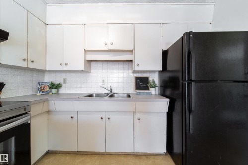 The kitchen features white cabinetry, a tiled backsplash, a double basin sink, and a black refrigerator - 3518 78 Street, Edmonton, AB - Indoor Photo Showing Kitchen With Double Sink