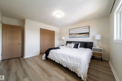 This bedroom features light wood-look flooring, a window providing natural light, and a closet with bi-fold doors - 3518 78 Street, Edmonton, AB - Indoor Photo Showing Bedroom