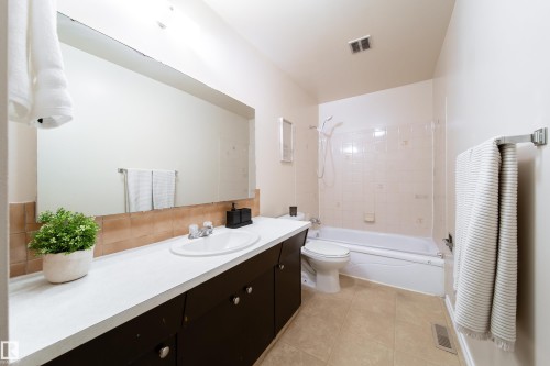 Bathroom featuring a white vanity with an integrated sink, a rectangular mirror, and a full-size bathtub with a shower - 3518 78 Street, Edmonton, AB - Indoor Photo Showing Bathroom