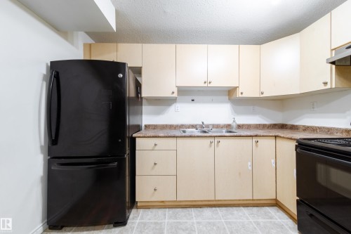 The property features a kitchen with light-colored cabinetry, a black refrigerator, a black stove, and a double basin sink - 3518 78 Street, Edmonton, AB - Indoor Photo Showing Kitchen With Double Sink