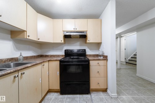 The kitchen features light wood cabinetry, a double basin stainless steel sink, and a black electric range with an overhead exhaust fan - 3518 78 Street, Edmonton, AB - Indoor Photo Showing Kitchen