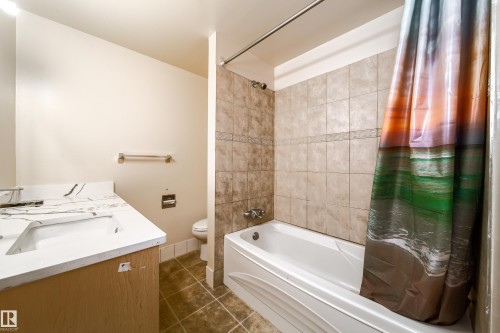 The bathroom features a vanity with a white countertop and an integrated sink, a toilet, a shower-tub combination with tiled walls, and tile flooring - 3518 78 Street, Edmonton, AB - Indoor Photo Showing Bathroom