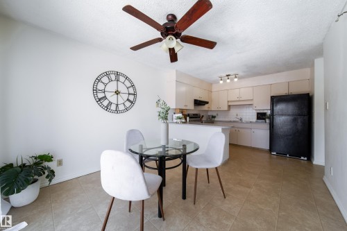 Bright dining area and kitchen featuring tiled flooring, a ceiling fan, white cabinetry, and a black refrigerator - 3518 78 Street, Edmonton, AB - Indoor