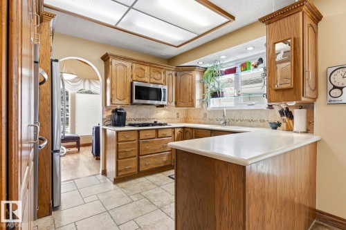 Kitchen featuring wood cabinetry, stainless steel appliances, a tile backsplash, light-toned countertops, and tile flooring - 11707 29 Avenue Nw, Edmonton, AB - Indoor Photo Showing Kitchen