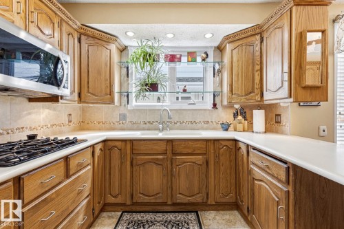 U-shaped kitchen with wood cabinetry featuring decorative trim, white countertops, and a tile backsplash with a decorative border - 11707 29 Avenue Nw, Edmonton, AB - Indoor Photo Showing Kitchen