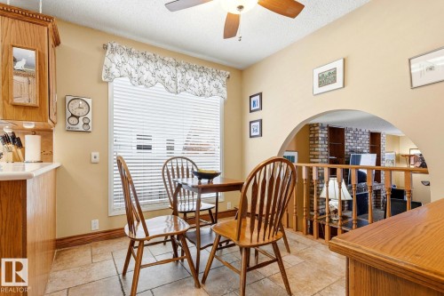 Dining area featuring a ceiling fan, window with blinds, wood-finish cabinetry, tile flooring, and an arched entryway with a wood railing - 11707 29 Avenue Nw, Edmonton, AB - Indoor Photo Showing Dining Room