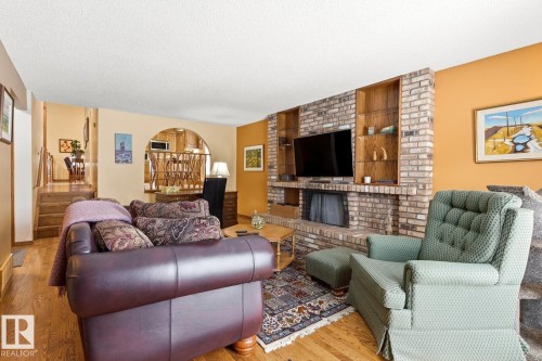 Living area featuring a brick-surround fireplace with hearth, integrated wooden shelving, and wood-finish flooring - 11707 29 Avenue Nw, Edmonton, AB - Indoor Photo Showing Living Room