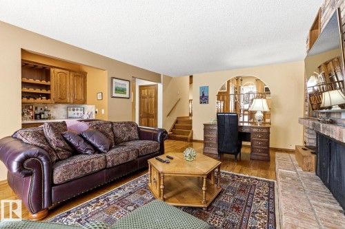 Living area featuring hardwood flooring, a built-in wet bar with wood cabinetry, a brick fireplace, and an arched entryway - 11707 29 Avenue Nw, Edmonton, AB - Indoor Photo Showing Living Room With Fireplace