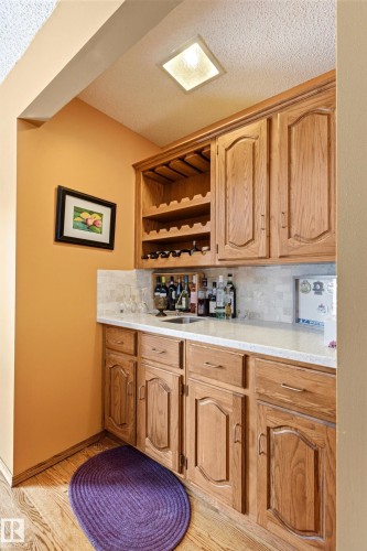 Built-in wet bar featuring wood-finish cabinetry, integrated wine storage, a stainless steel sink, and light-toned countertops with a tiled backsplash - 11707 29 Avenue Nw, Edmonton, AB - Indoor Photo Showing Other Room