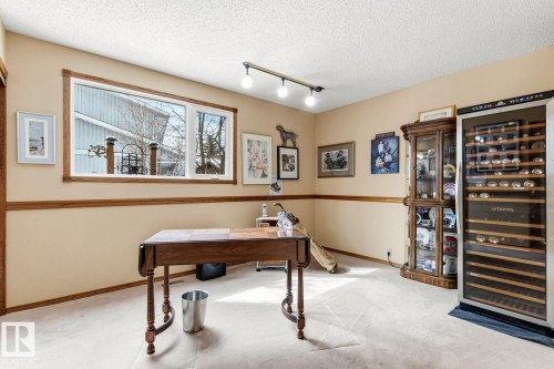 Spacious room featuring neutral carpeting, light beige walls with wood trim, a large window, a built-in display cabinet, and track lighting - 11707 29 Avenue Nw, Edmonton, AB - Indoor Photo Showing Other Room