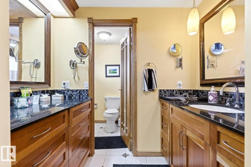 Dual wood-finish vanities with dark countertops and tiled backsplashes - 11707 29 Avenue Nw, Edmonton, AB - Indoor Photo Showing Bathroom