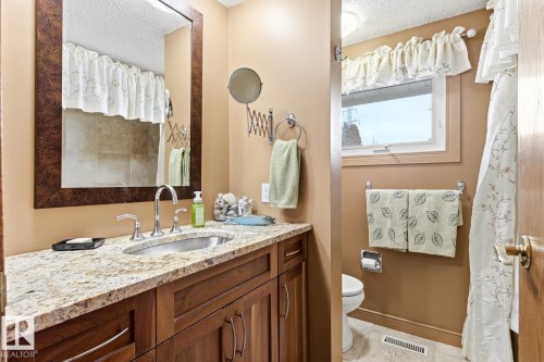 Vanity featuring an undermount sink with a chrome faucet, a stone countertop, and wood cabinetry - 11707 29 Avenue Nw, Edmonton, AB - Indoor Photo Showing Bathroom