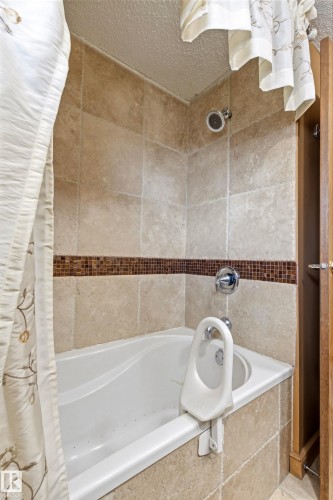 White bathtub with chrome fixtures, surrounded by light-toned tile walls and a decorative mosaic accent band - 11707 29 Avenue Nw, Edmonton, AB - Indoor Photo Showing Bathroom