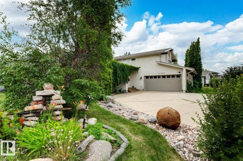 Stucco exterior property featuring an attached two-car garage, concrete driveway, and mature landscaping with decorative rock beds - 11707 29 Avenue Nw, Edmonton, AB - Outdoor