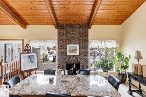 Spacious room featuring a prominent brick fireplace with an arched opening, a wood-paneled ceiling with exposed beams, and large windows providing natural illumination - 11707 29 Avenue Nw, Edmonton, AB - Indoor Photo Showing Dining Room