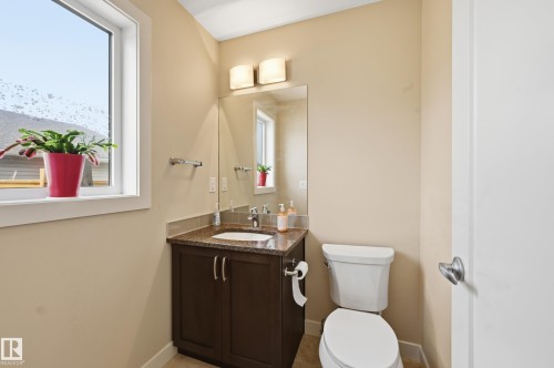 This bathroom features a white toilet, a dark wood vanity with a granite countertop and an undermount sink, and a large mirror - 701 Allard Boulevard, Edmonton, AB - Indoor Photo Showing Bathroom