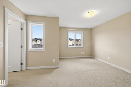 This room features neutral-toned carpet, light beige walls, and two windows providing natural light - 701 Allard Boulevard, Edmonton, AB - Indoor Photo Showing Other Room