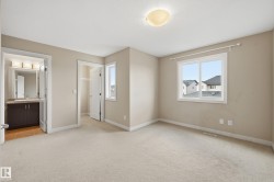 This room features neutral-toned carpet flooring, a window offering views of nearby rooftops, and a flush mount ceiling light fixture - 