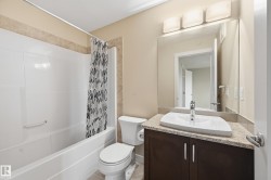 Well-appointed bathroom featuring a white bathtub, a toilet, and a vanity with a rectangular sink and dark cabinetry - 
