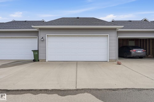 The property features garages with white panel doors and an attached concrete driveway - 701 Allard Boulevard, Edmonton, AB - Outdoor With Exterior