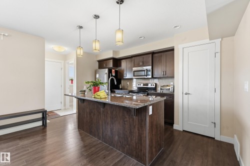The kitchen features dark wood cabinetry, stainless steel appliances, a granite countertop island with a sink, and dark wood flooring - 701 Allard Boulevard, Edmonton, AB - Indoor Photo Showing Kitchen With Upgraded Kitchen