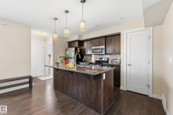 The kitchen features dark wood cabinetry, stainless steel appliances, a granite countertop island with a sink, and dark wood flooring - 
