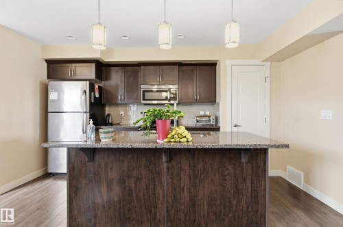 The kitchen features a dark wood island with a granite countertop, pendant lighting, and stainless steel appliances including a refrigerator and microwave - 701 Allard Boulevard, Edmonton, AB - Indoor Photo Showing Kitchen With Upgraded Kitchen