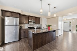 The kitchen features stainless steel appliances, dark wood cabinetry, and a granite island with a sink - 