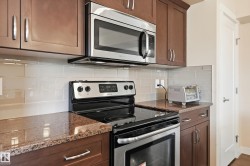The kitchen features granite countertops, a subway tile backsplash, and stainless steel appliances including a microwave and an oven with an electric stovetop - 