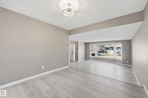 This spacious room features light-colored flooring, neutral wall paint, and a modern ceiling light fixture - 6907 19 Avenue, Edmonton, AB - Indoor