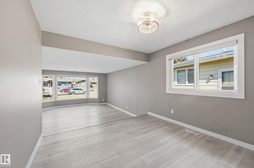 Spacious living area featuring light-toned flooring, neutral walls, and ample natural light from large windows - 6907 19 Avenue, Edmonton, AB - Indoor Photo Showing Other Room