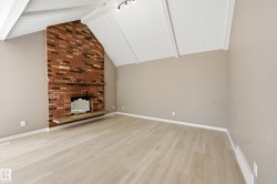 Living area featuring light-colored flooring, a brick fireplace with a hearth, and a vaulted ceiling - 