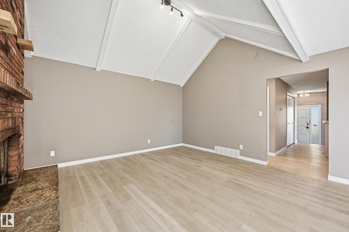 The living area features a vaulted ceiling with exposed beams, light-toned flooring, and a brick fireplace - 6907 19 Avenue, Edmonton, AB - Indoor Photo Showing Other Room With Fireplace