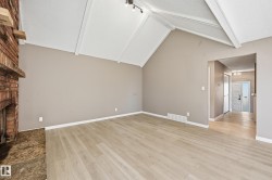 The living area features a vaulted ceiling with exposed beams, light-toned flooring, and a brick fireplace - 