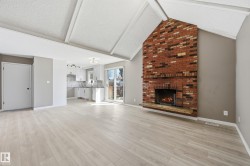 The living area features vaulted ceilings, light-toned flooring, and a brick fireplace with a hearth - 