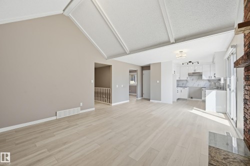 Spacious living area featuring light-toned flooring, vaulted ceilings, and an exposed brick fireplace - 6907 19 Avenue, Edmonton, AB - Indoor