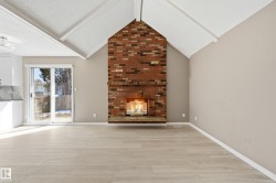 Living area featuring a prominent brick fireplace, light-colored flooring, and a vaulted ceiling - 