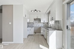 The kitchen features white cabinetry with black hardware, a light-colored countertop, and a matching backsplash - 