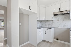 The kitchen features white cabinetry with black hardware, dark countertops, and a white marble-patterned backsplash - 
