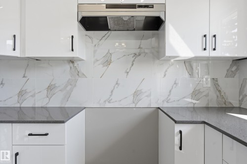 The kitchen features white cabinetry with dark hardware, a stainless steel range hood, stone countertops, and a white and grey patterned tile backsplash - 6907 19 Avenue, Edmonton, AB - Indoor Photo Showing Kitchen