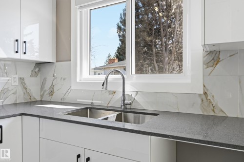 Kitchen featuring white cabinetry, a double basin stainless steel sink, a modern faucet, and a tiled backsplash - 6907 19 Avenue, Edmonton, AB - Indoor Photo Showing Kitchen With Double Sink