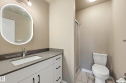 The bathroom features a vanity with a rectangular undermount sink, a gray countertop, and a lighted oval mirror - 