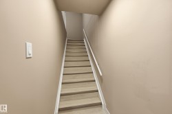 Staircase featuring light-toned wooden steps, white risers, and a white handrail, set against neutral-colored walls - 