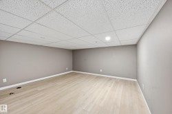 Expansive room featuring light-colored flooring, neutral-toned walls, and a white grid ceiling with recessed lighting - 