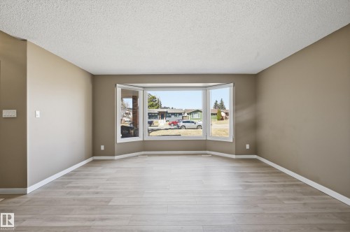 This inviting living area features light-colored plank flooring, neutral wall paint, and a large bay window, providing ample natural light - 6907 19 Avenue, Edmonton, AB - Indoor Photo Showing Other Room