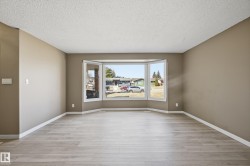 This inviting living area features light-colored plank flooring, neutral wall paint, and a large bay window, providing ample natural light - 